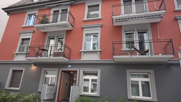 A multi-story building with balconies, a ground entrance, and a visible door. - Centrally located 2BR (Color 23) (Zürich)