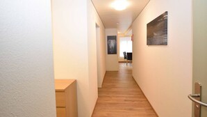 A narrow hallway with wooden flooring, white walls, and a door on the right. There is a small wooden desk on the left and a framed picture on the wall. - Centrally located 2BR (Color 23) (Zürich)