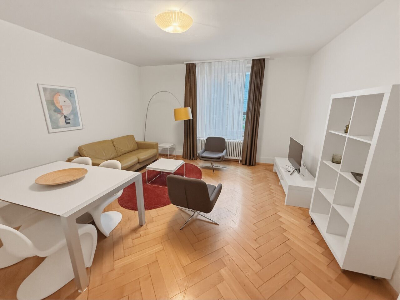 A modern living room with a sofa, a dining table, a TV, and a bookshelf.