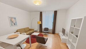 A modern living room with a sofa, a dining table, a TV, and a bookshelf. - 2BR near lake (Stardust 11) (Zürich)
