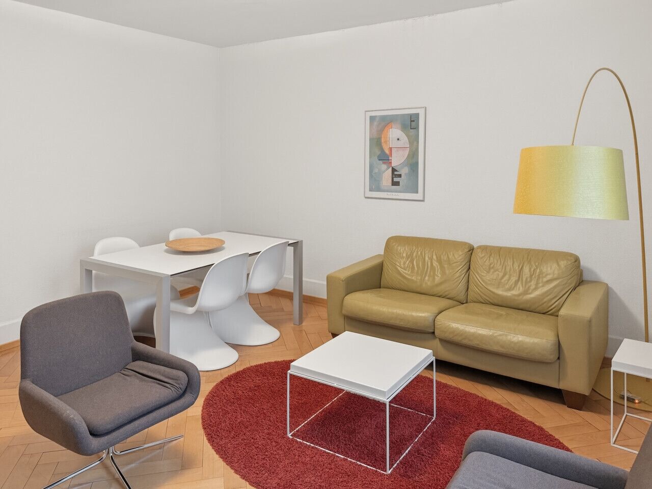 A modern living room with a grey armchair, a beige sofa, a white coffee table, and a red rug.