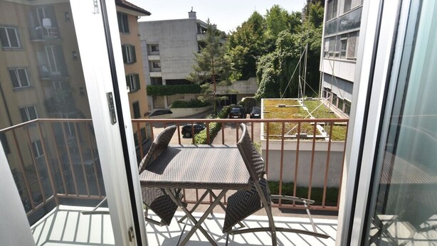 Un balcon avec une table et des chaises, donnant sur un quartier résidentiel avec des immeubles et des voitures garées.