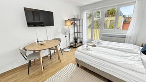 Hotellihuone, jossa on sänky, seinälle asennettu televisio, pyöreä pöytä tuoleineen ja lattiavalaisin.