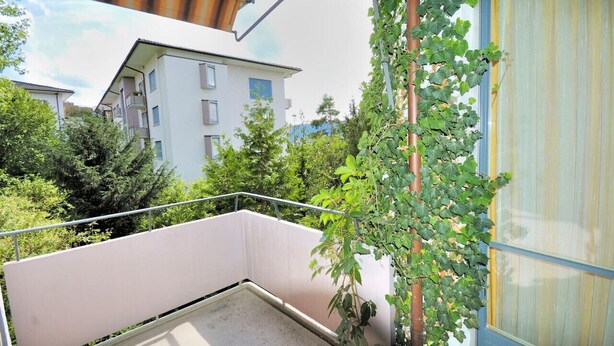 A balcony with a view of neighboring buildings and greenery.