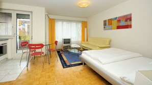 A compact hotel room with a bed, a small desk with a chair, a television, and a sofa.