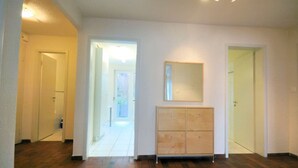 A spacious hallway with a wooden cabinet and a mirror on the wall, leading to a door and a bright room.