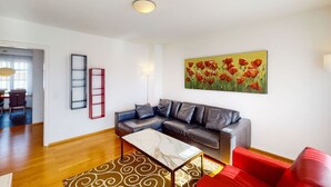 A modern living room with a sectional sofa, a coffee table, and a vibrant painting of red flowers.