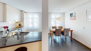 A modern kitchen with a black countertop and stainless steel appliances. There is a dining area with a wooden table and chairs.
