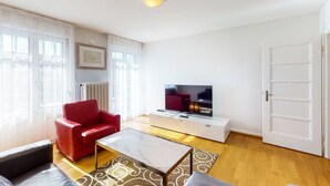 A modern living room with a red sofa, a glass coffee table, a TV on a white cabinet, and a door to the right.