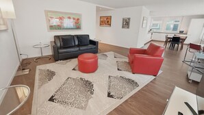 Ein modernes Wohnzimmer mit einer schwarz-roten Sofagarnitur, einem großen gemusterten Teppich und einem Essbereich im Hintergrund.