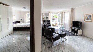Ein modernes Hotelzimmer mit einem Bett, einer Sitzecke mit Sessel und kleinem Tisch, einem Fernseher und Blick ins Freie.