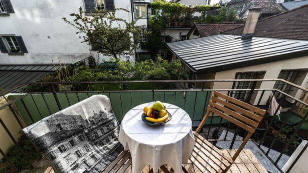 Ein Balkon mit rundem Tisch, einem Stuhl und einer Decke.