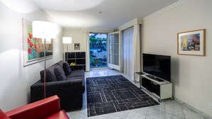 Ein modernes Wohnzimmer mit einer Couch, einem Fernseher auf einem Schrank und Blick durch eine Glastür nach draußen.