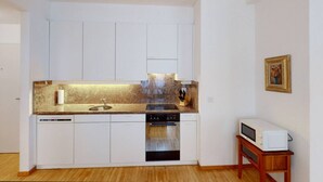 A compact kitchen with white cabinets, a stainless steel sink, a built-in oven, and a microwave on a wooden stand. - Nice 1BR apartment near lake (FB6) (Zürich)