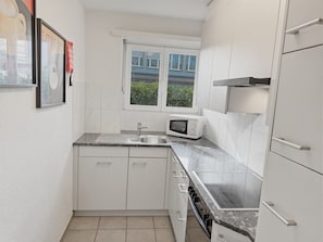 A compact kitchen with white cabinets, a granite countertop, a microwave, and a window with a view of greenery outside.