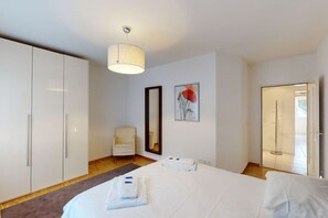 A hotel room with a large bed, a wardrobe, a chair, a mirror, and a shower area. - Executive 1BR flat, city center (Hammer 1) (Zürich)
