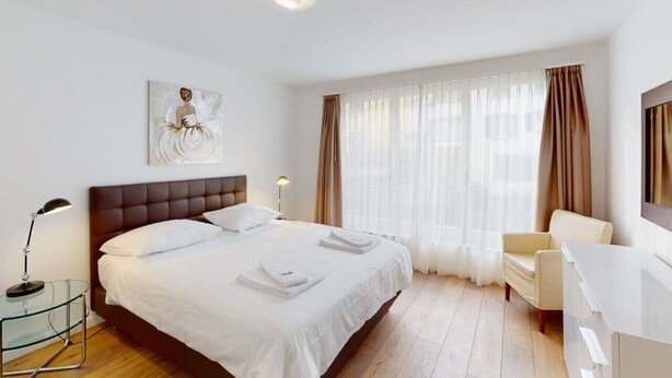 Una habitación de hotel con una cama grande, un escritorio, una silla, una mesita de noche, una lámpara y un cuadro en la pared.