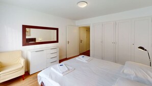 Una habitación de hotel con cama, mesita de noche, lámpara, armario y espejo.