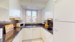 A modern kitchen with white cabinets, a granite countertop, a microwave, and a sink.