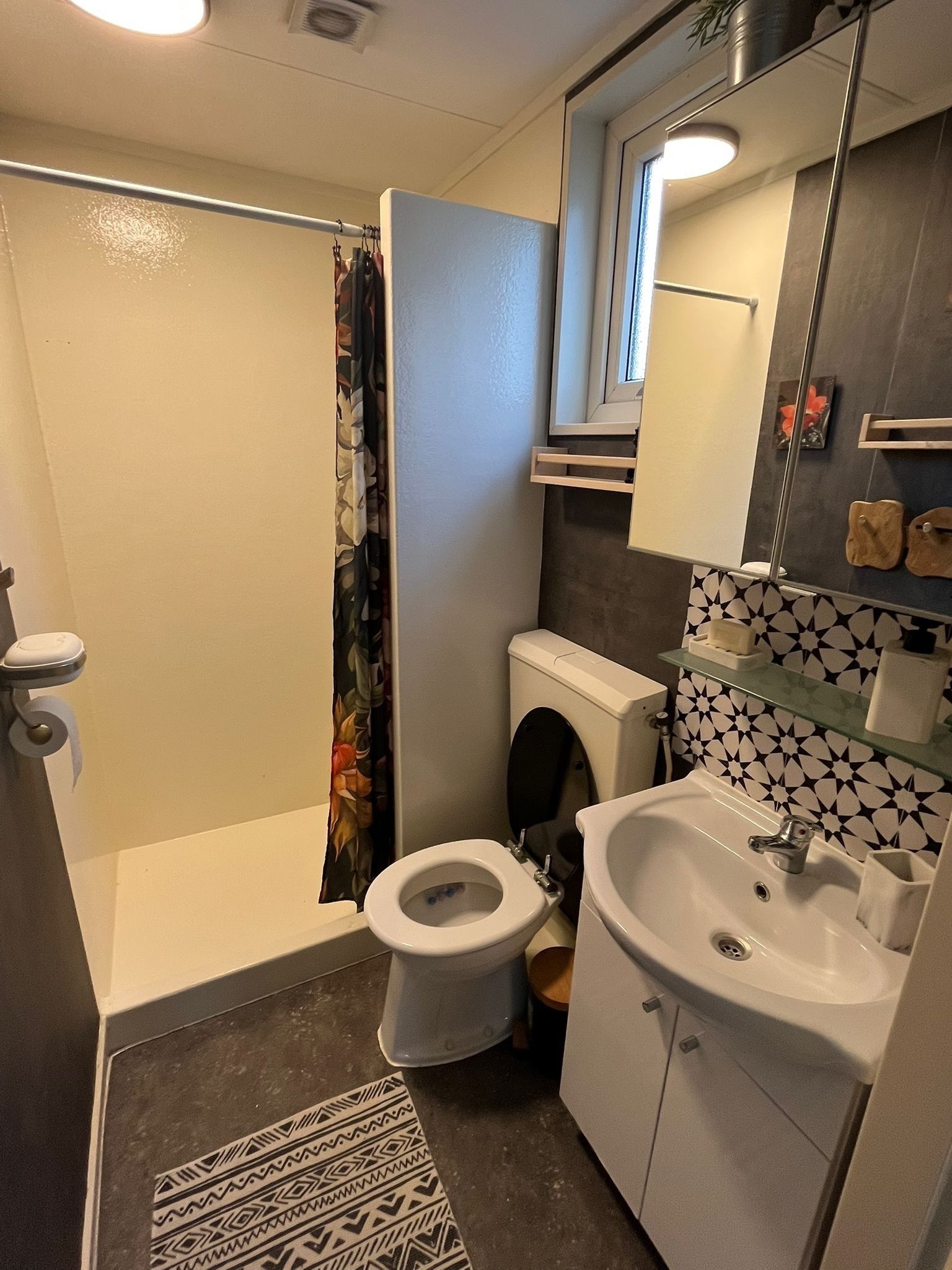 Un baño compacto con ducha, inodoro, lavamanos y espejo sobre el lavamanos.