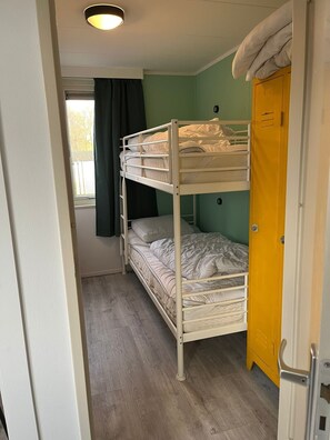 Une chambre avec un lit superposé, un plancher en bois, une fenêtre avec des rideaux et une porte jaune.