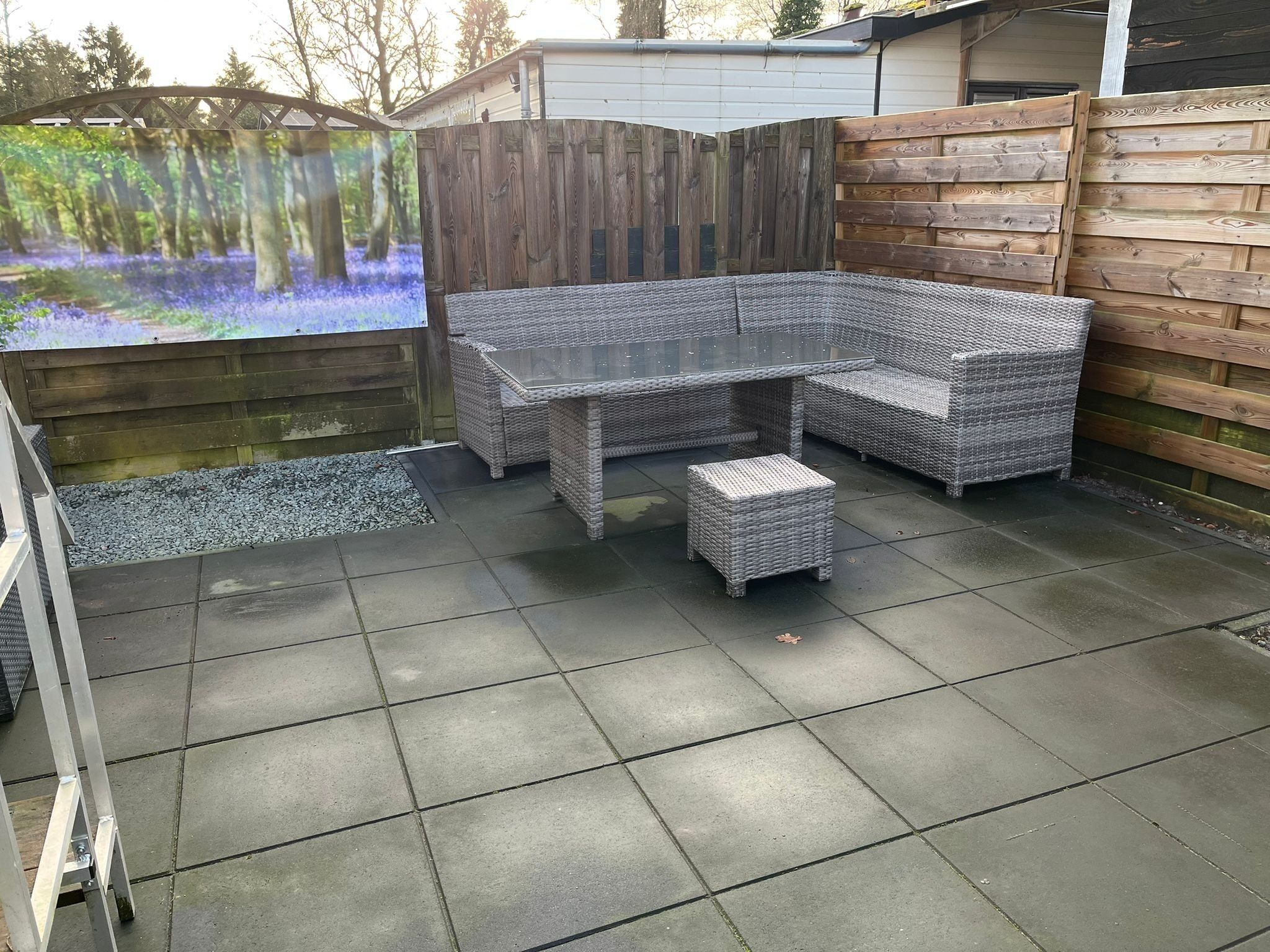 Un espace extérieur aménagé en terrasse, avec un canapé d'angle en rotin, une table à plateau en verre et un petit pouf.