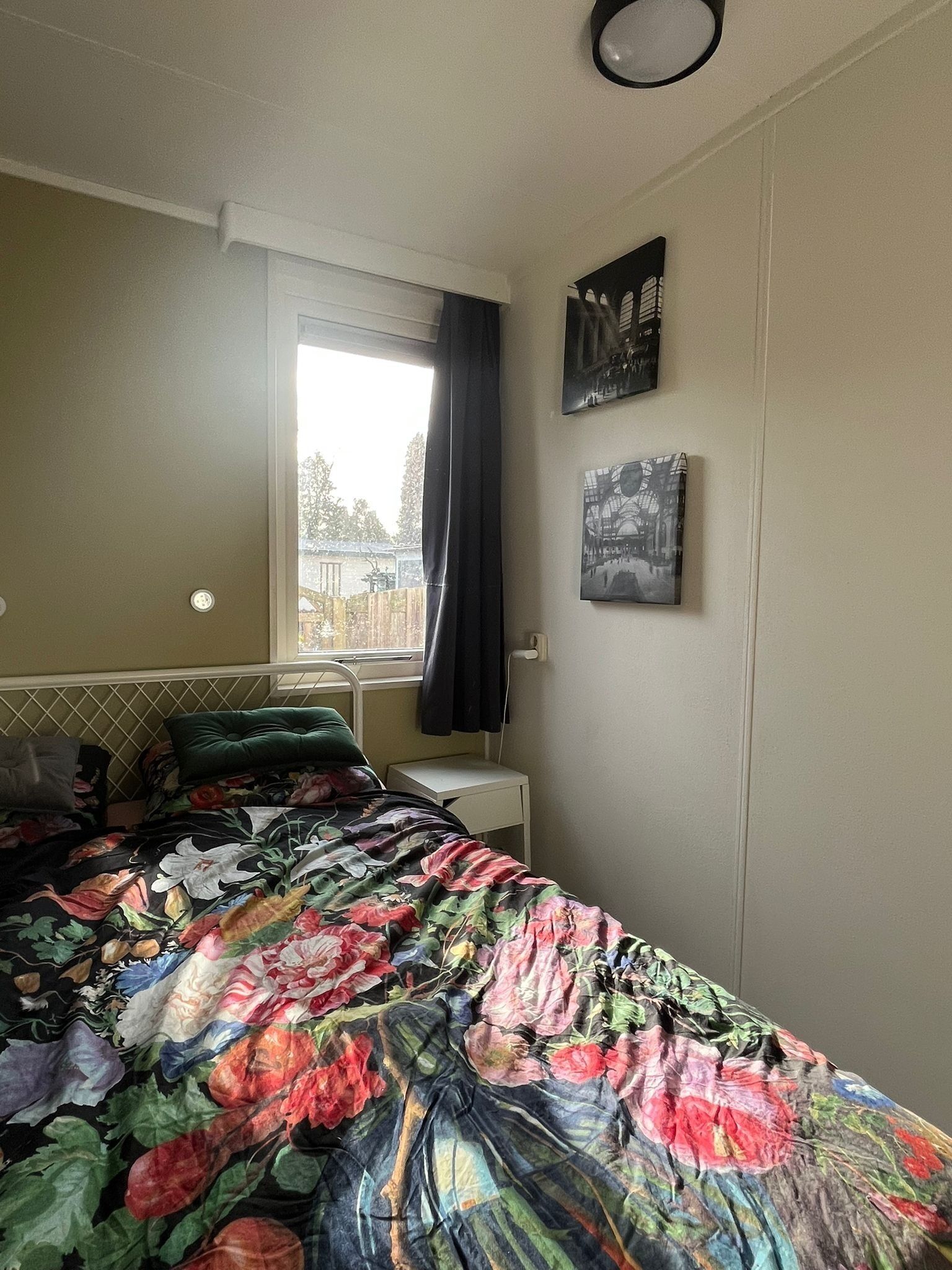 Une chambre à coucher avec un lit, une fenêtre avec des rideaux, une table de chevet et des œuvres d’art murales.