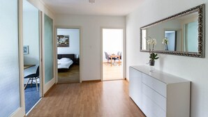 A hotel room with a wooden floor, a white dresser, a large mirror, and a bed in the background. - Bright 1 BR flat (Parkview 1) (Zürich)
