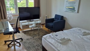 A hotel room with a bed, a desk with a chair, a TV, and a blue armchair.