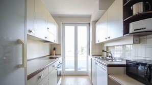 A narrow kitchen with white cabinets, a microwave, and a sink.