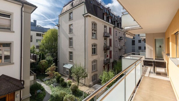 A residential building with a balcony, a garden area, and neighboring buildings.