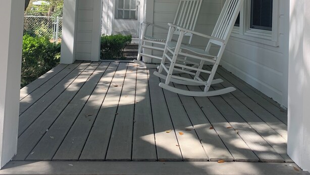 Een veranda met witte houten leuningen en een schommelstoel.