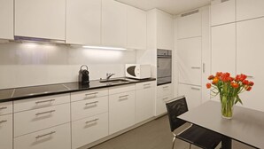 Una cocina moderna con armarios blancos, una encimera negra, microondas integrado y horno de acero inoxidable. Hay un jarrón con flores rojas en la mesa de comedor.