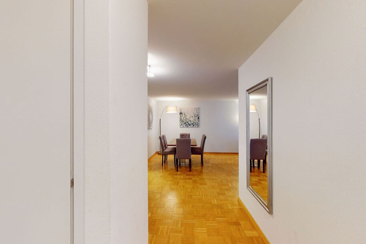 Ein Flur, der in einen Essbereich mit Holzboden, einem Tisch mit Stühlen und einem Spiegel an der Wand führt.