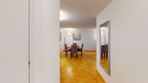 Un pasillo que conduce a un comedor con suelo de madera, una mesa con sillas y un espejo en la pared.