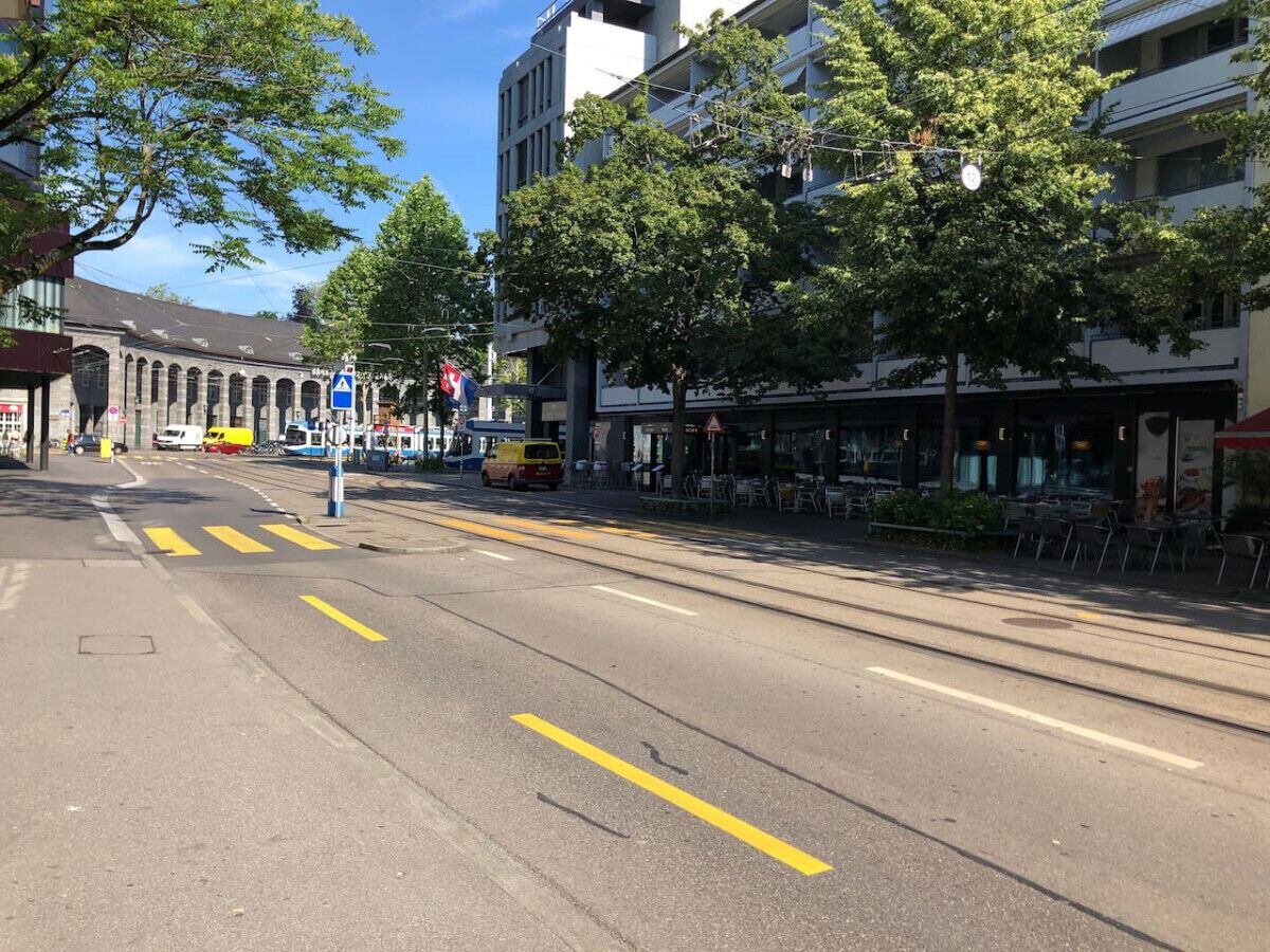 A street with a tram track, buildings, and a café on the right.