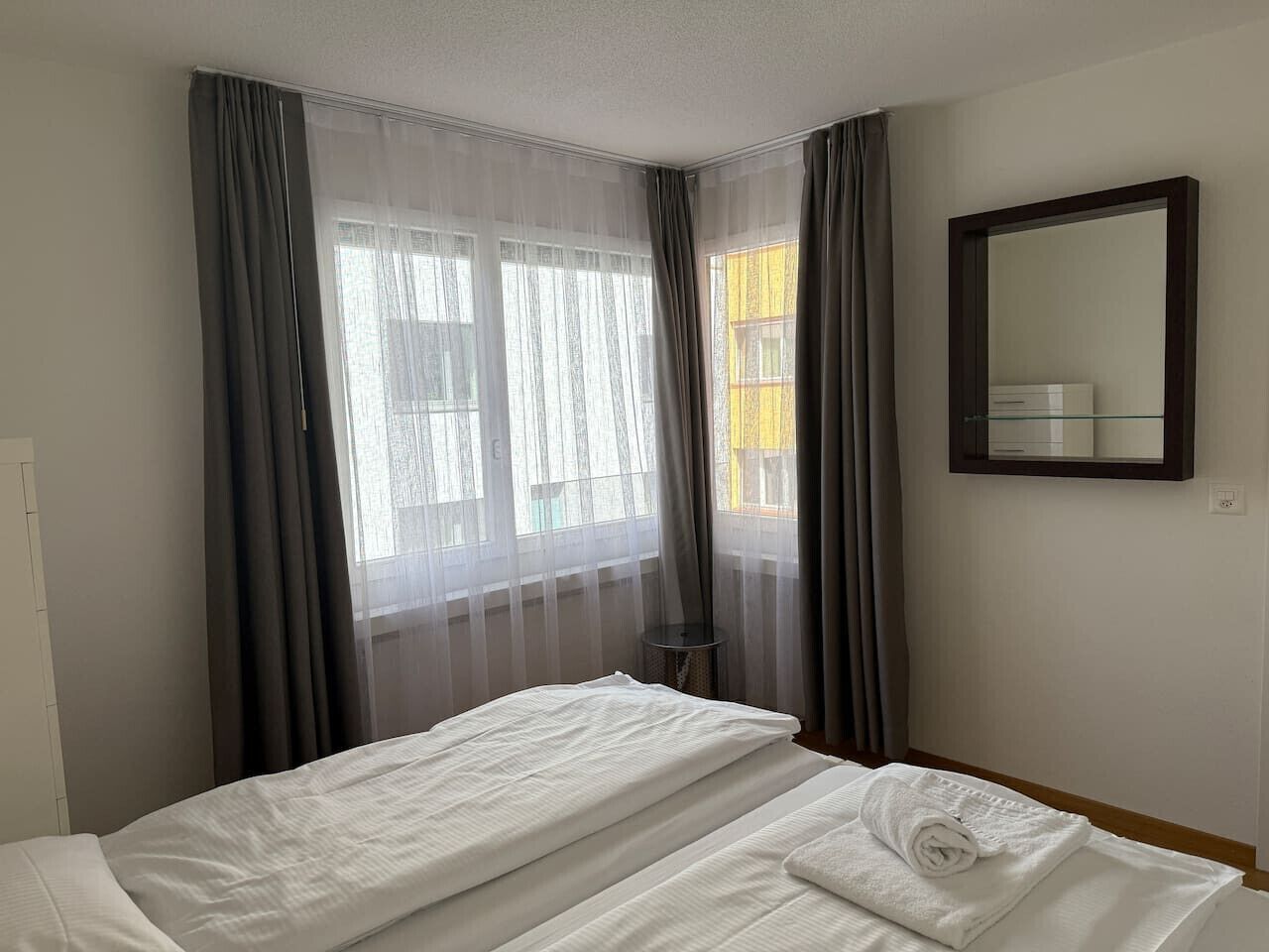 A hotel room with a bed, a mirror, and sheer curtains.
