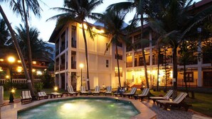 A pool area with lounge chairs and a hot tub, surrounded by palm trees and a building with multiple balconies. - Le Huynh Mui Ne Hotel (Mui Ne)