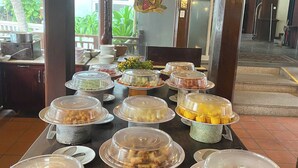 A buffet setup with various food items covered in plastic containers, a sign indicating 'Quay Khai Vi Appetizer Counter', and a view of the outdoors. - Le Huynh Mui Ne Hotel (Mui Ne)