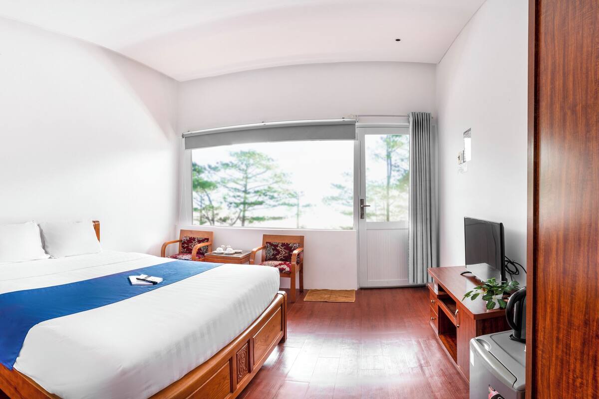 Un dormitorio con cama, mesita de noche de madera, escritorio, silla y televisor.