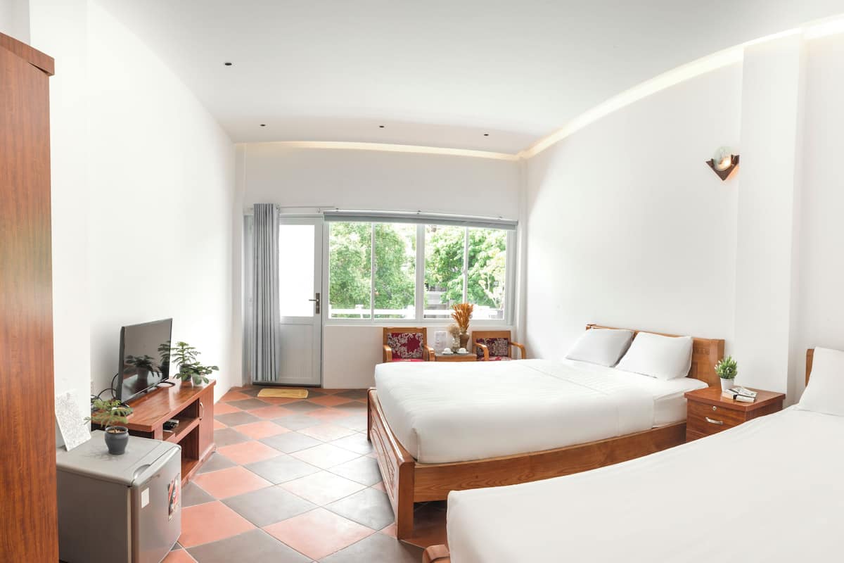 Habitación de hotel moderna con dos camas, un televisor, un escritorio y ventana con vista a zonas verdes.