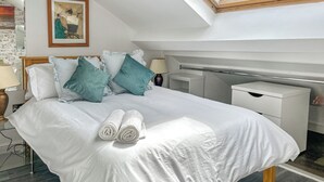 A neatly made bed with rolled towels, a bedside table with a lamp, a small bedside table, and a nightstand.