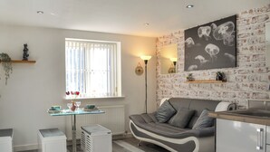 A modern kitchen with a grey sofa, a dining table, and a large window with curtains.