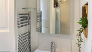 Un bagno con un lavandino bianco, uno spazio doccia in vetro e un portasciutto in metallo.