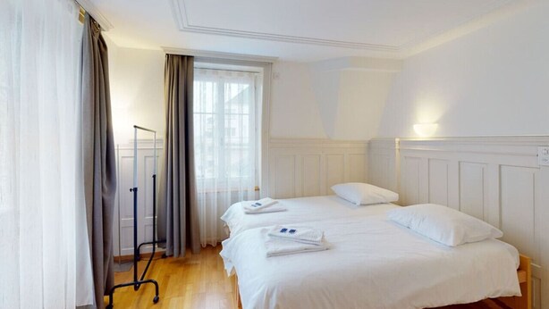 A hotel room with two beds, a window with curtains, a standing lamp, and a wooden floor. - Penthouse flat in the city center/near lake (SF18) (Zürich)