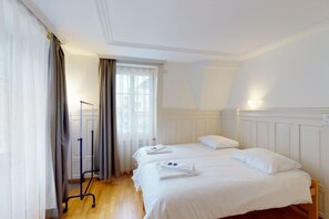 A hotel room with two beds, a window with curtains, a standing lamp, and a wooden floor.