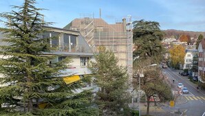 Une vue de rue avec un bâtiment en construction, un passage piéton et des véhicules sur la chaussée.