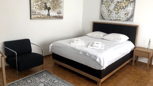 Une chambre avec un lit, une chaise noire, un plancher en bois et deux œuvres d’art murales.