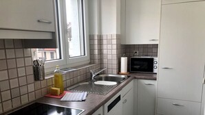 Une cuisine compacte avec une plaque de cuisson noire, un évier, un four à micro-ondes et des placards blancs.