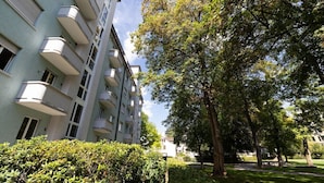 A multi-story residential building with balconies, surrounded by lush greenery and trees.